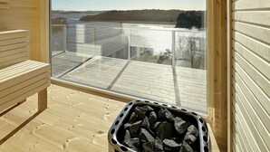 A sauna room with a wooden bench and a glass-enclosed window overlooking a body of water and a forested area.