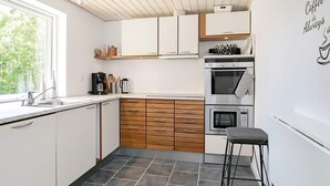 A modern kitchen with white cabinets, a wooden countertop, and a bar stool. - Holiday Home in LÃ¦sÃ¸ (Læsø)