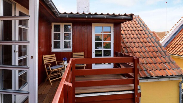 Eine Holzterrasse mit roter Geländer, einem Tisch mit Stühlen und einem Fenster mit Blick auf die Nachbarschaft.