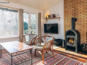 A living room with a fireplace, a television, wicker chairs, a wooden table, and a patterned rug. - 4 Person Holiday Home in Vejby (Vejby)