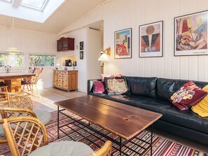 A cozy living room with a wooden coffee table, a black leather sofa, and a dining area with a wooden cabinet and chairs. - 4 Person Holiday Home in Vejby (Vejby)