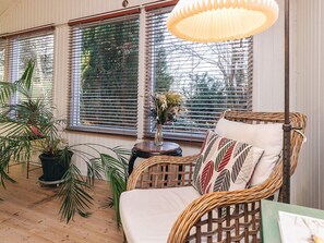 A wicker chair with cushions, a potted plant, and a vase with flowers on a wooden floor. - 4 Person Holiday Home in Vejby (Vejby)