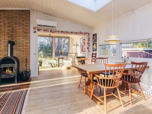 A cozy interior with a brick fireplace, wooden dining table, and chairs, surrounded by large windows and a view of the outdoors. - 4 Person Holiday Home in Vejby (Vejby)