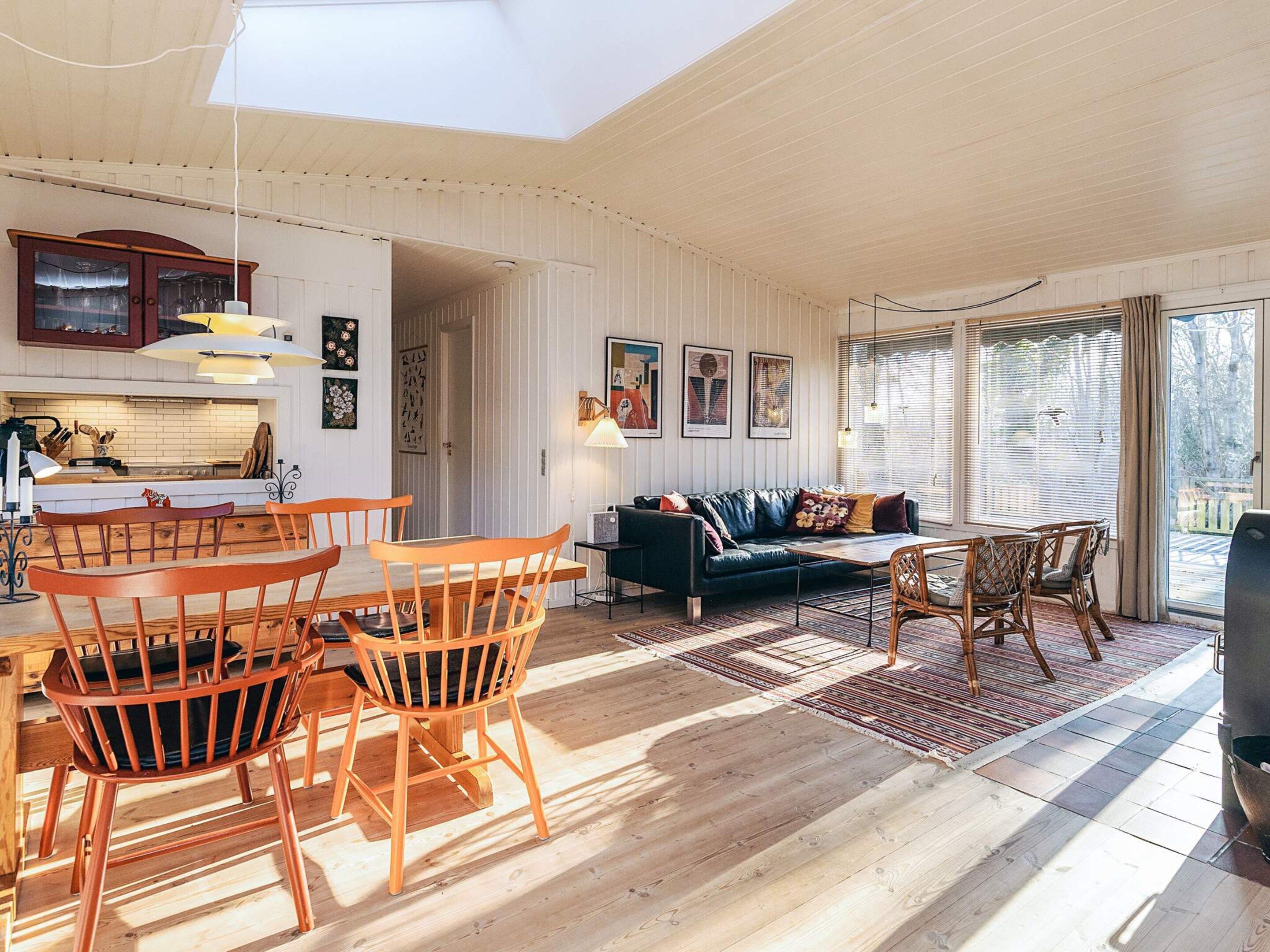 A spacious living room with a dining area, a black leather sofa, wooden chairs, and a large window with blinds.