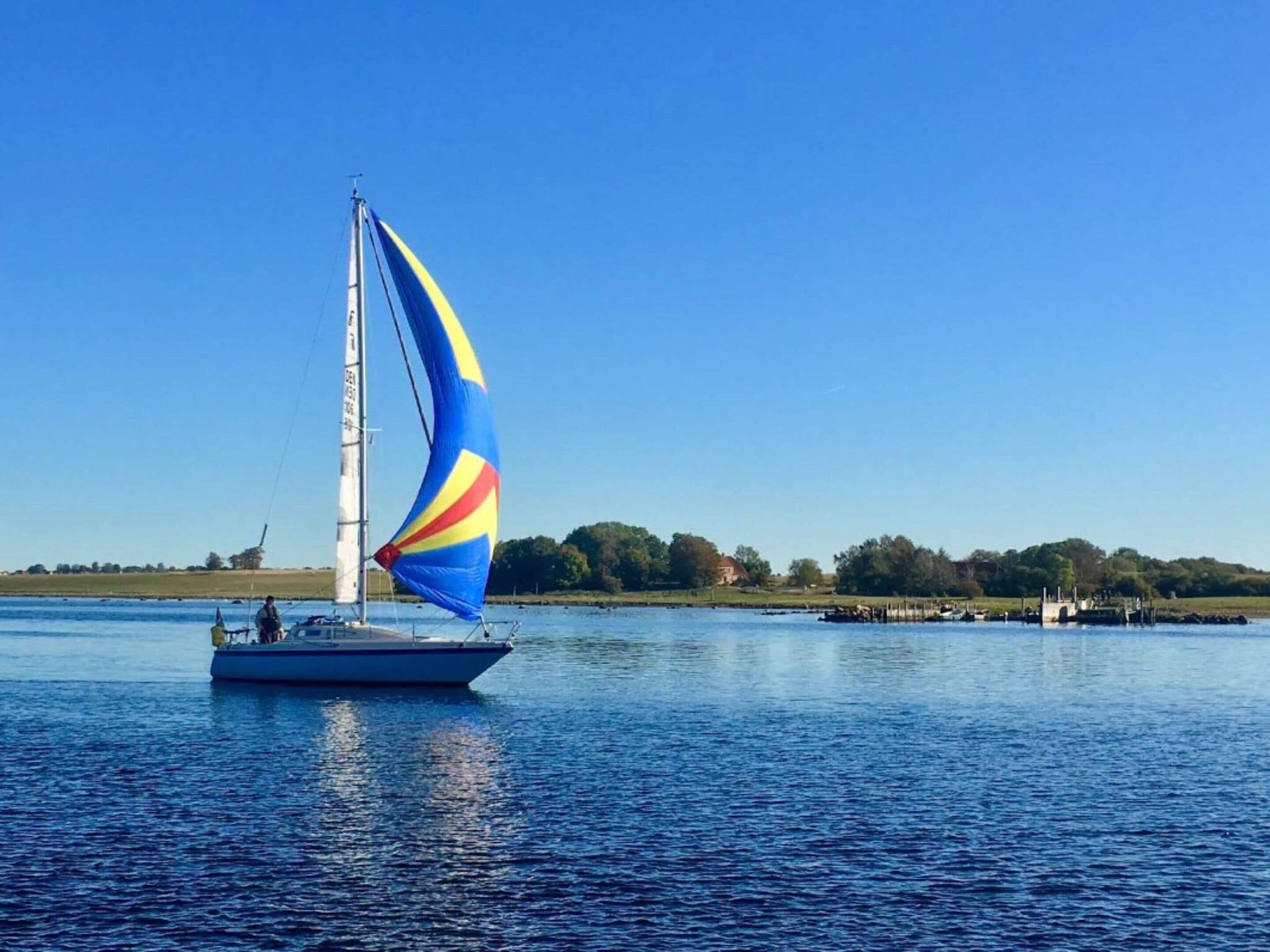 A sailboat with a colorful sail on a calm body of water.