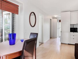 Comedor con una mesa, sillas y un vaso azul. Cocina con gabinetes blancos y un microondas.
