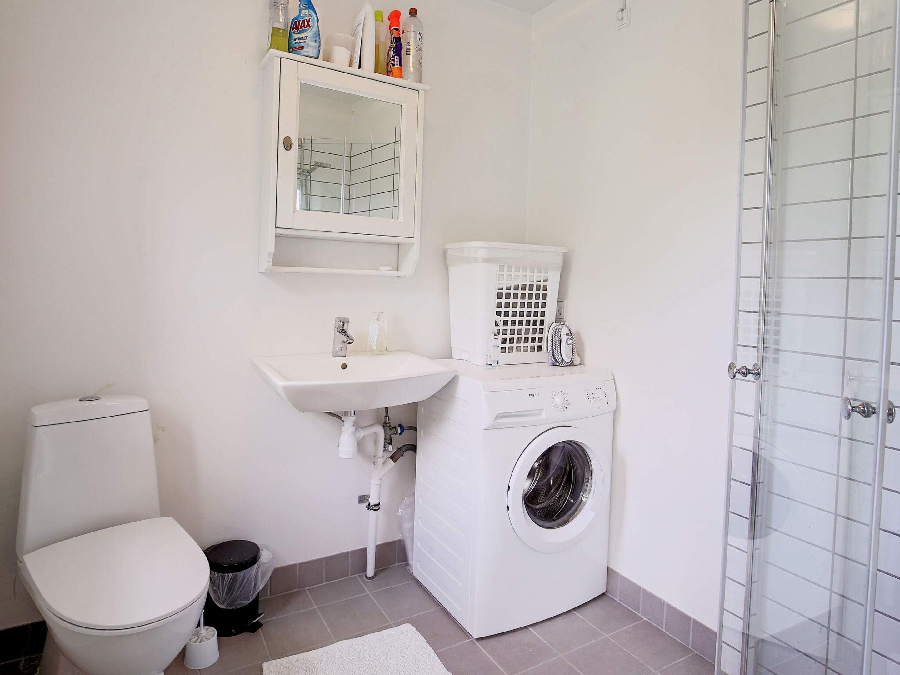 A compact bathroom with a toilet, sink, washing machine, and a glass shower enclosure.