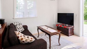 Ein Wohnzimmer mit einer Couch, einem Couchtisch, einem Flachbildfernseher und einer Holzkassette mit elektronischen Geräten.