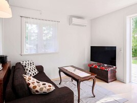Una sala de estar con un sofá, una mesa de centro, un televisor de pantalla plana y un mueble de madera con dispositivos electrónicos.