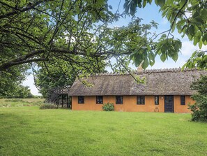 A traditional thatched-roof house with a grassy yard and a wooden staircase leading to a deck. - 4 Star Holiday Home in Rudkobing (Rudkobing)