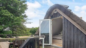 Een knus vakantiehuis met rieten dak en een schuifdeur naar een bed, gelegen op een houten terras met tuinmeubilair.