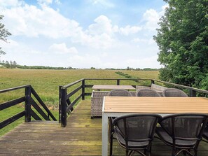 A wooden deck with a table and chairs, overlooking a grassy field.