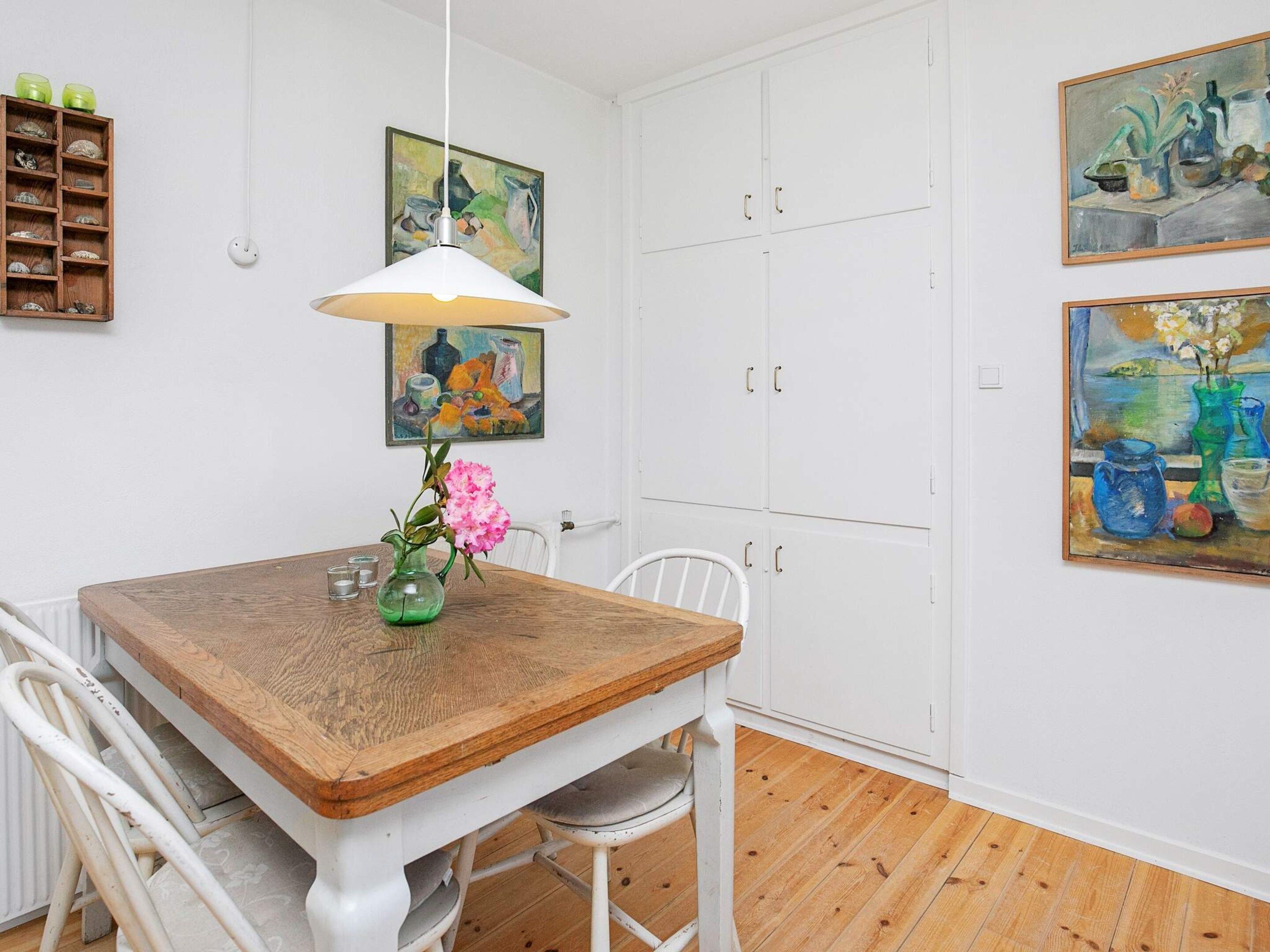 A dining area with a wooden table, white chairs, a hanging lamp, and artwork on the walls.