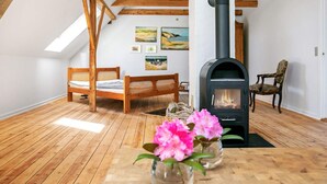 Un dormitorio acogedor en el ático con vigas de madera, una cama, una silla, una mesa con flores y un estufa de leña.