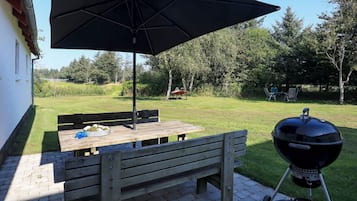 Une terrasse extérieure avec une table et un banc en bois, un parasol noir et un barbecue.