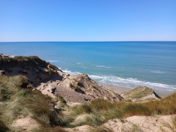 A coastal landscape with sandy dunes and a clear view of the ocean.