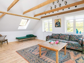 A loft-style room with a sloped ceiling, wooden beams, a green sofa, a patterned rug, and a painting on the wall. - 6 Person Holiday Home in Hjorring (Hjørring)