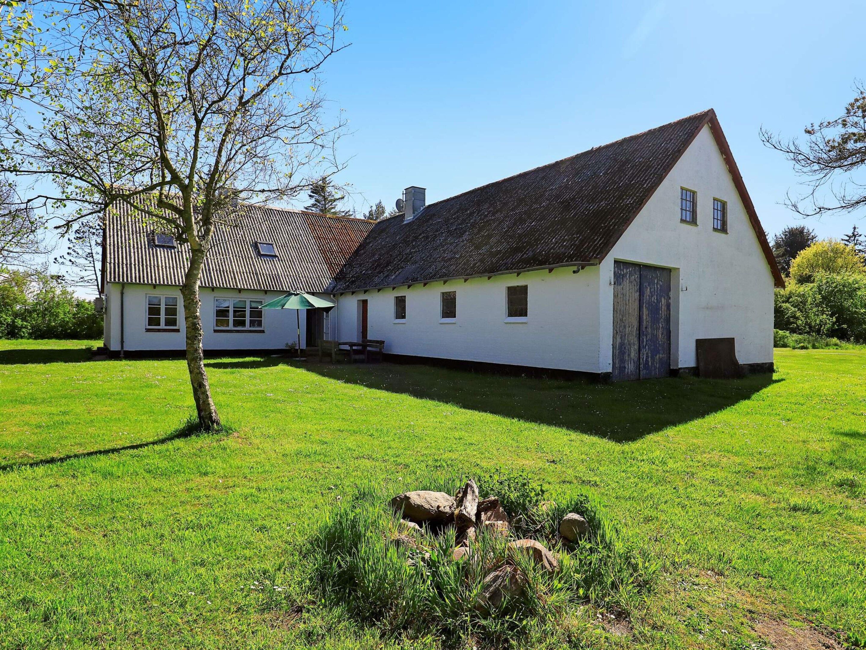 En hvid bygning med skrå tag, stor åben gårdsplads og et træ i forgrunden.