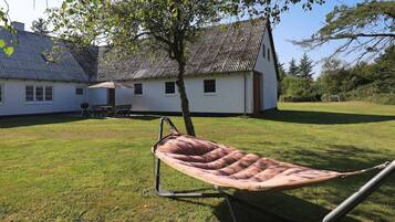 Una hamaca en un jardín con césped y una casa al fondo.