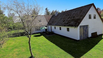 A white building with a sloped roof, a green umbrella, and a grassy yard.