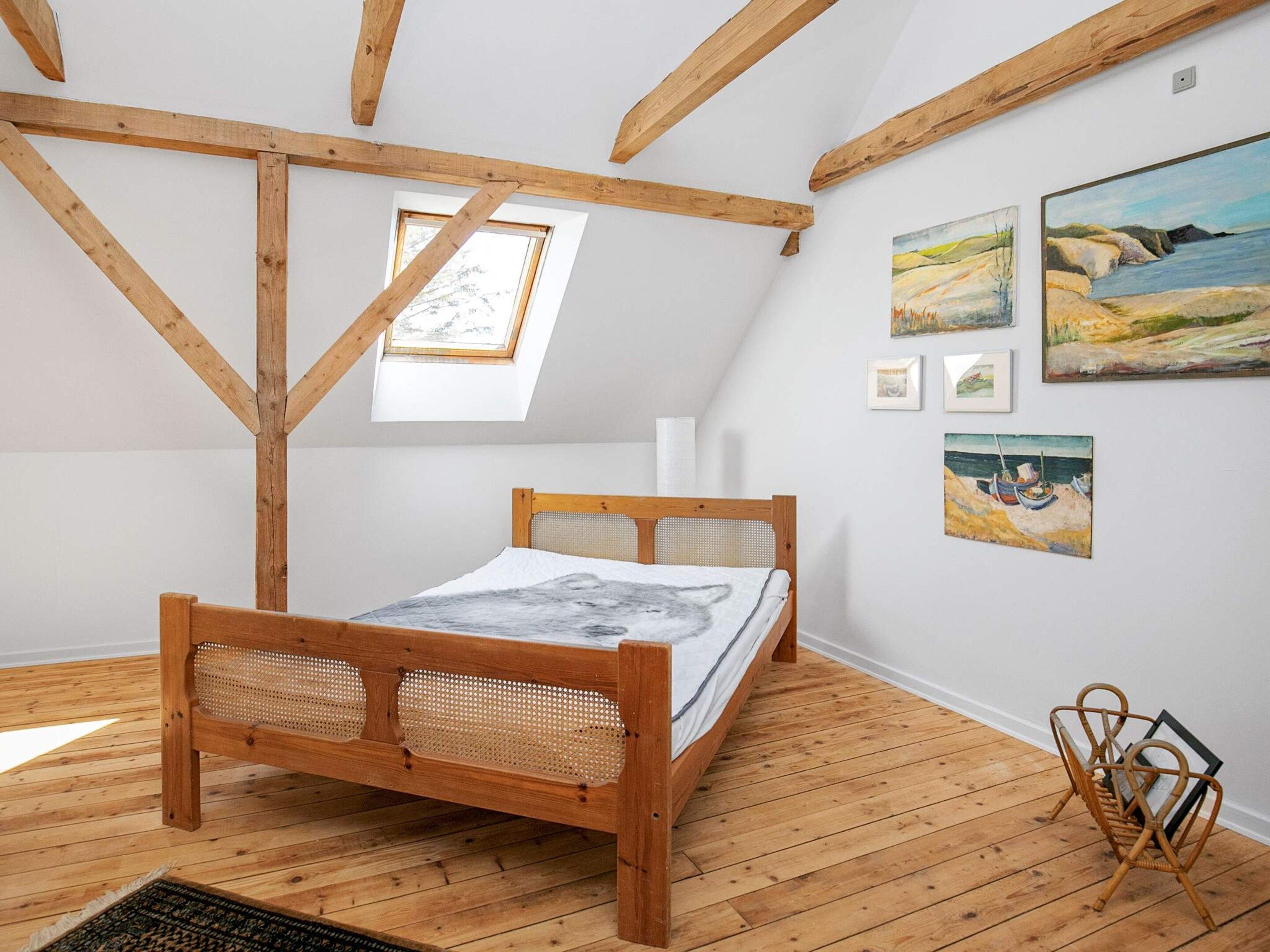 A bedroom with a wooden bed, a skylight, and artwork on the walls.