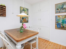 Un comedor con mesa de madera, sillas blancas, una lámpara colgante y obras de arte en las paredes.