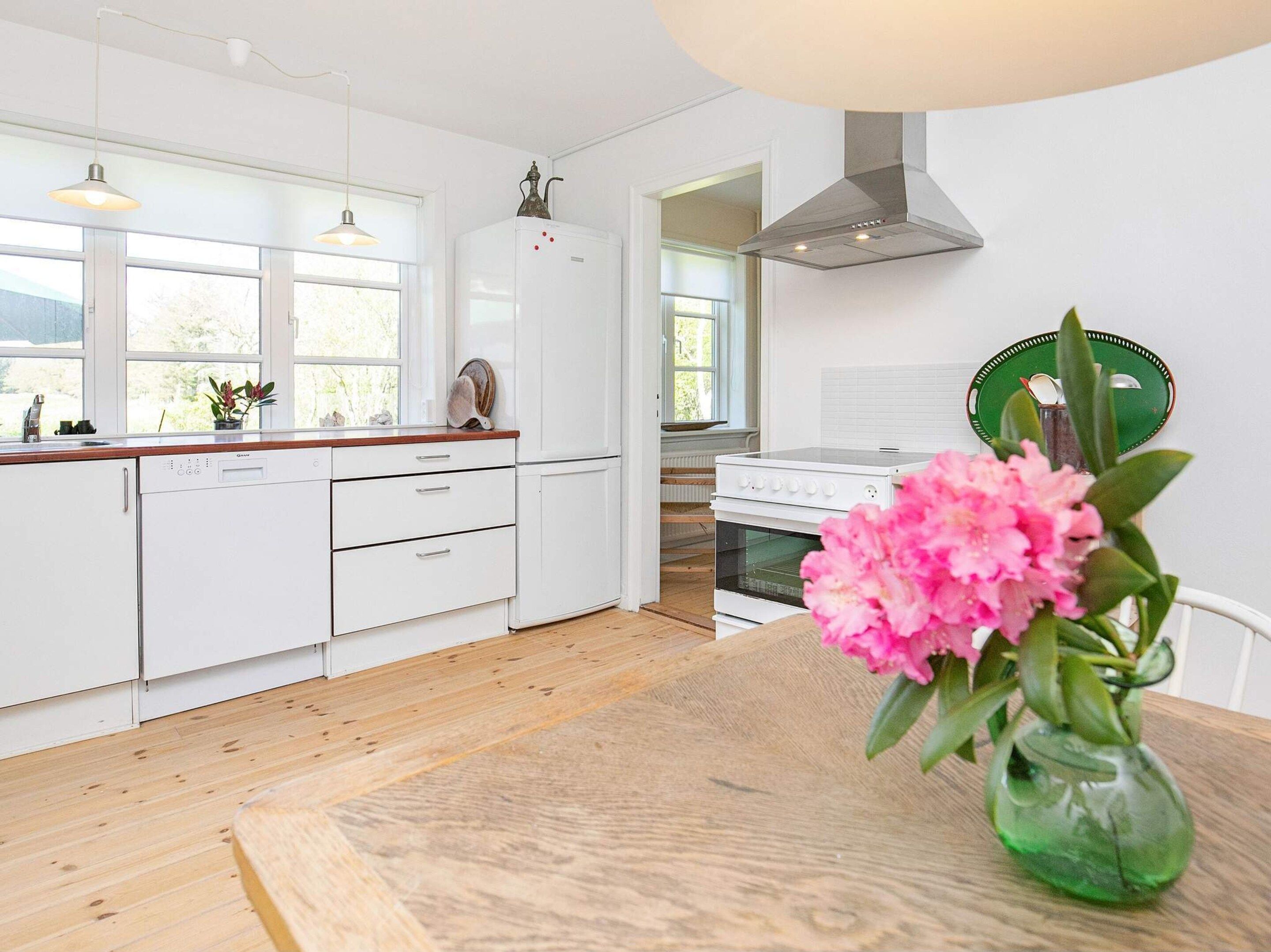Et moderne køkken med hvide skabe, en træbordplade, en opvaskemaskine, en ovn og en grøn vase med blomster på et træbord.