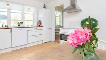 Une cuisine moderne avec des meubles blancs, un plan de travail en bois, un lave-vaisselle, un four et un vase vert orné de fleurs, posé sur une table en bois.
