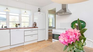 Una cocina moderna con armarios blancos, encimera de madera, lavavajillas, horno y un florero verde con flores sobre una mesa de madera.