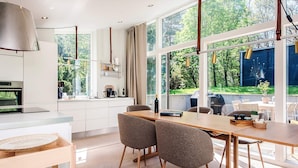 Een moderne keuken met een eethoek, grote ramen en uitzicht op groen.