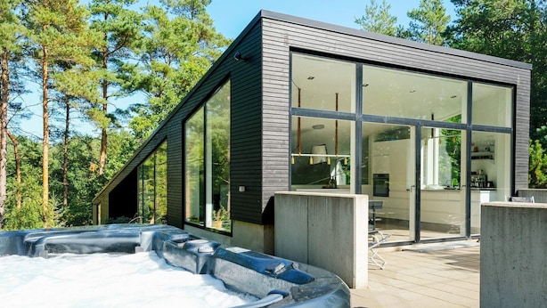 Een moderne buitenjacuzzi met een houten terras, omringd door een houten blokhut met grote glasramen.
