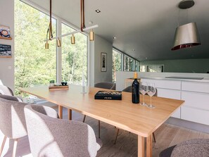 A modern dining area with a wooden table, chairs, and a view of greenery outside.