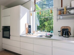 A modern kitchen with white cabinetry, a built-in oven, a coffee maker, and a window with a view of greenery.