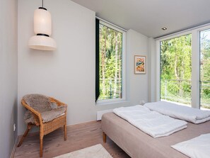 A bedroom with a bed, a chair, a window, and a pendant light.