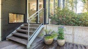 Een modern huis met een houten terras, een trap en twee grote potplanten.