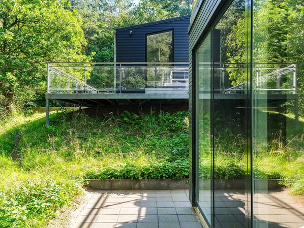 A modern building with a glass facade, a metal bridge, and lush greenery.