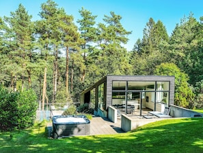 A modern house with a hot tub, outdoor seating, and a view of a forest.