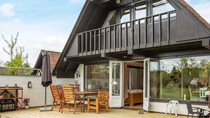 A modern house with a wooden deck, a dining area with chairs and a table, and a large sliding glass door leading to an interior space. - Holiday Home in VÃ¦ggerlÃ¸se (Vaeggerlose)
