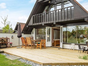 A modern house with a wooden deck, outdoor seating, and a glass door leading to an interior room. - Holiday Home in VÃ¦ggerlÃ¸se (Vaeggerlose)