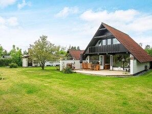 Et moderne hus med en stor terrasse, et spiseområde og en overdækket siddekrog.