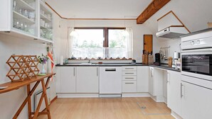 A modern kitchen with white cabinets, a wooden table, and a window with curtains. - Holiday Home in VÃ¦ggerlÃ¸se (Vaeggerlose)
