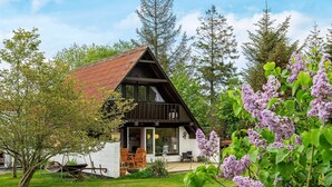 A cabin with a sloped roof, a deck, and a garden with trees and flowers. - Holiday Home in VÃ¦ggerlÃ¸se (Vaeggerlose)