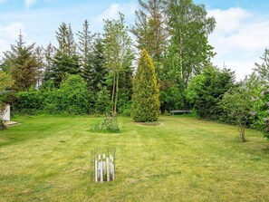 A well-maintained grassy area with a variety of trees and shrubs, a fenced garden bed, and a bench. - Holiday Home in VÃ¦ggerlÃ¸se (Vaeggerlose)