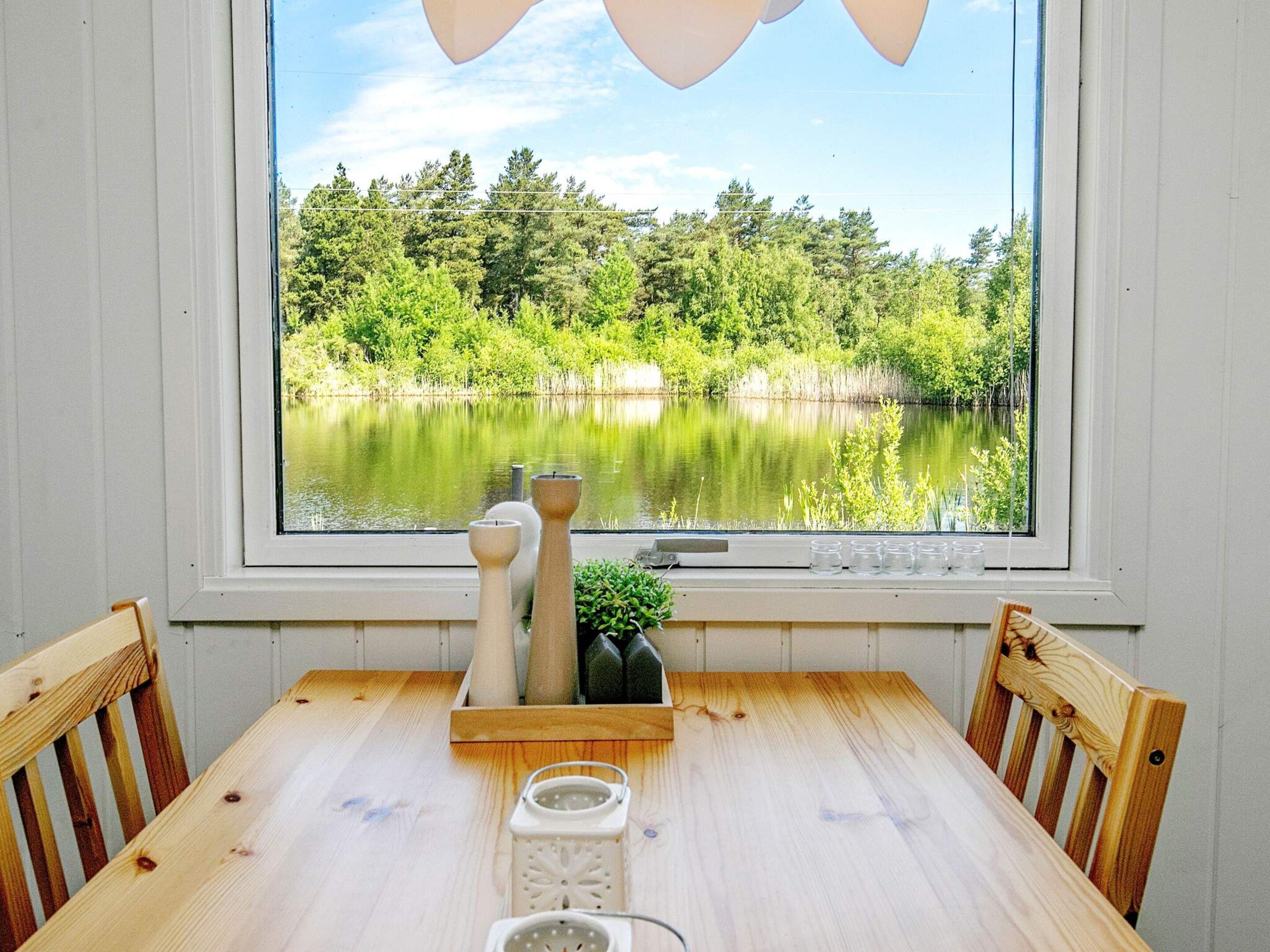 A wooden table with chairs, a window with a view of a lake and trees, and decorative items on the windowsill.