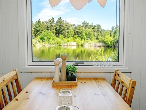 A wooden table with chairs, a window with a view of a lake and trees, and decorative items on the windowsill.