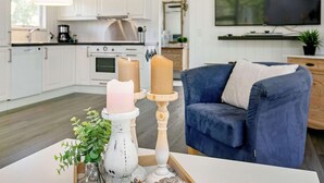 A modern kitchen with white cabinets, a stove, and a dining area with a blue sofa and a white table. - 4 Person Holiday Home in Laeso (Læsø)