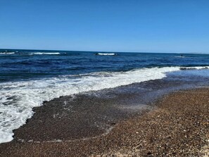 A beach with pebbles, waves, and a clear blue sky.