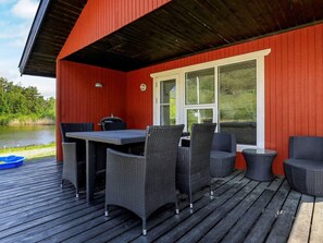 A covered outdoor area with a table and chairs, a window, and a view of a body of water.