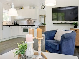Una cocina moderna con armarios blancos, una campana extractora de acero inoxidable y una zona de comedor con sofá azul y mesa blanca.
