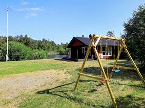 A wooden swing set in a grassy area with a house and a body of water in the background.